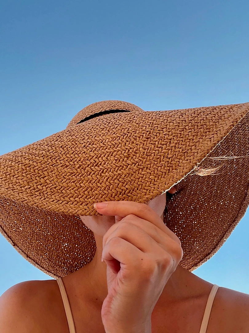 Femme protégeant son visage du soleil sous un grand chapeau de paille, précaution essentielle avant un soin visage à la lumière pulsée